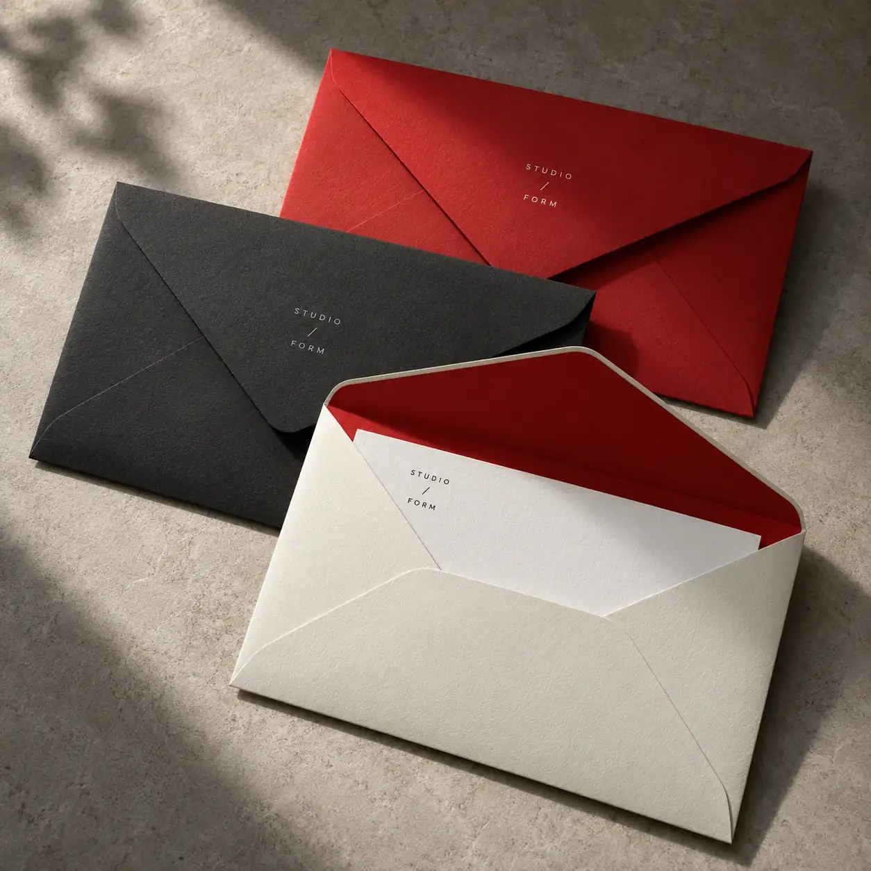 Printed envelopes shown as a physical product in charcoal, red and warm white