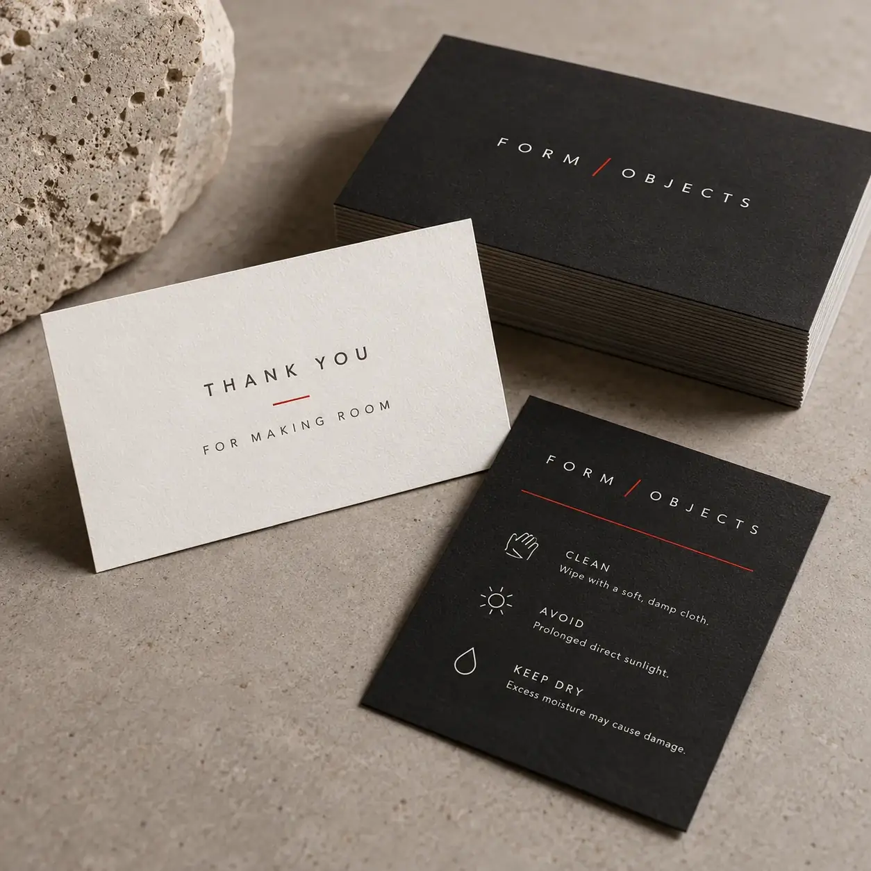 Printed packaging cards shown as a physical product in charcoal, red and warm white