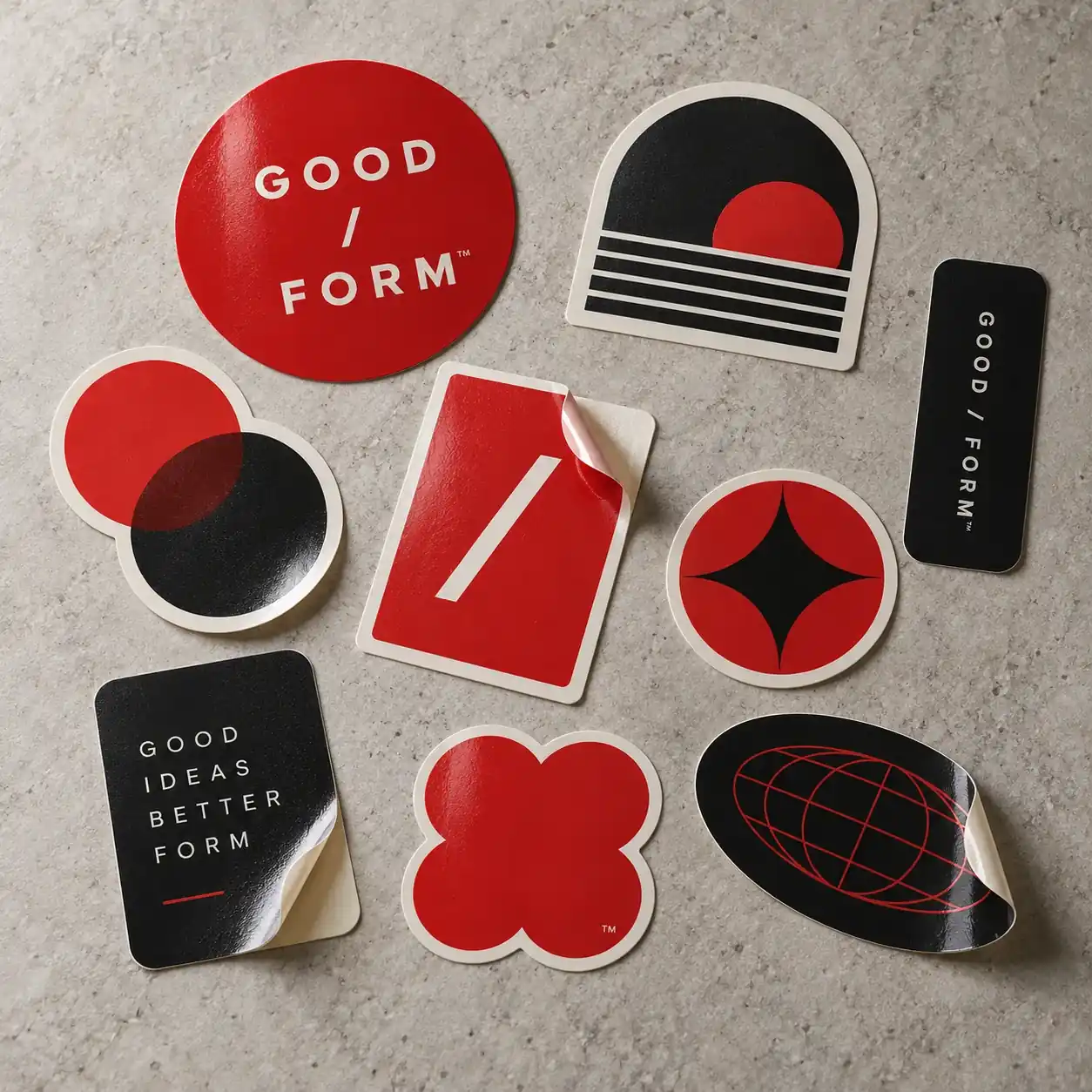 Printed stickers shown as a physical product in charcoal, red and warm white